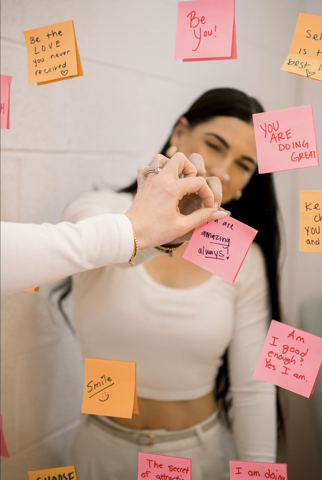 A woman putting sticky notes with positive affirmations on her mirror.