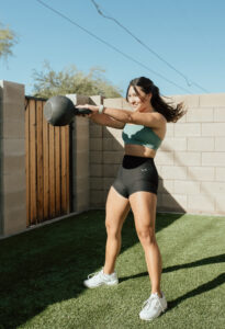 A female performing proper form when doing a kettlebell swing outside